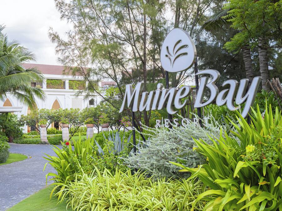 A sign for "Mune Bay Resort" surrounded by lush greenery and a pathway.