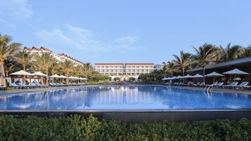 Zona de piscina hotelera con tumbonas, sombrillas y palmeras.