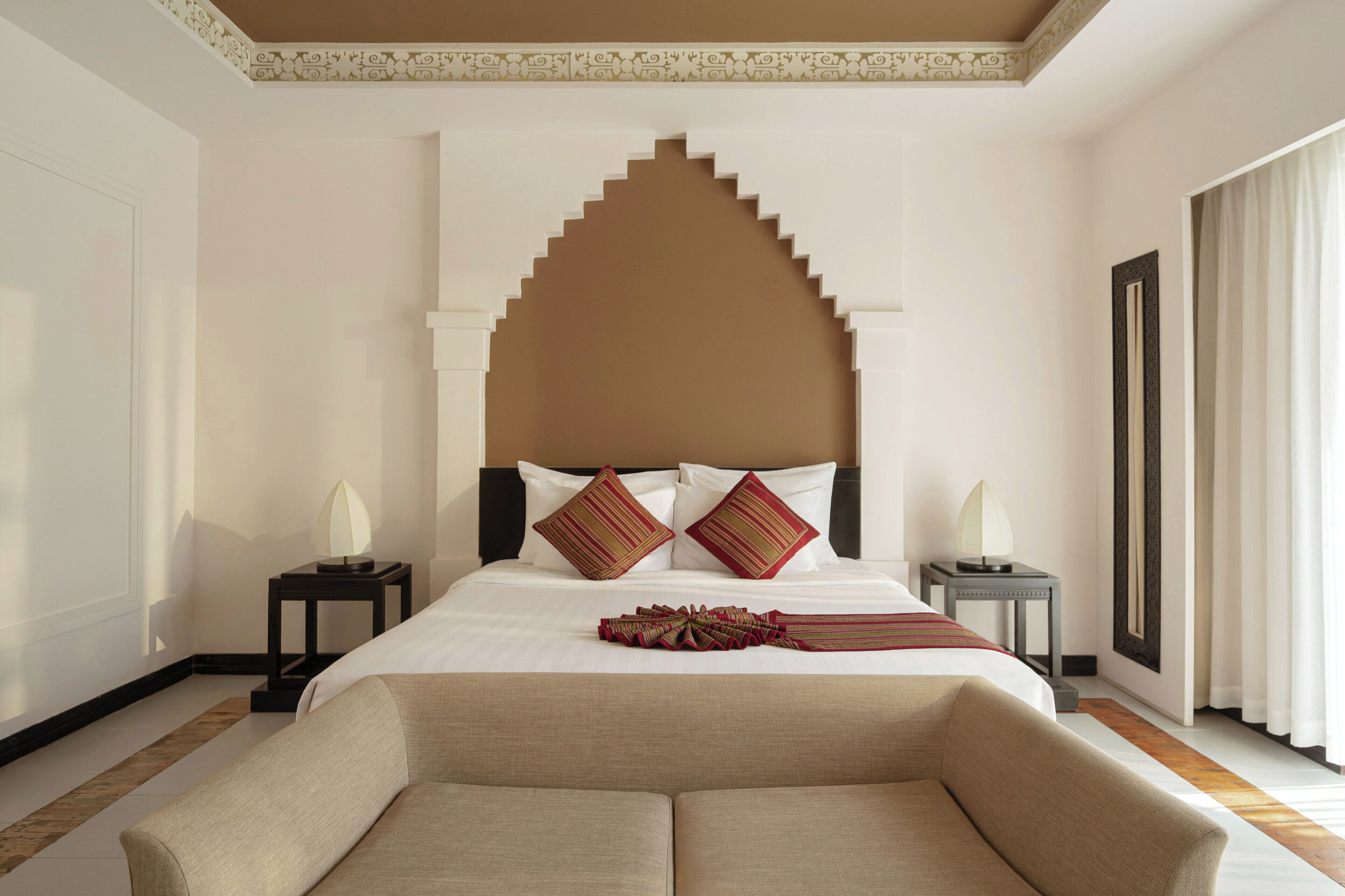 A hotel room with a large bed, two bedside tables, a decorative headboard, and a sofa.