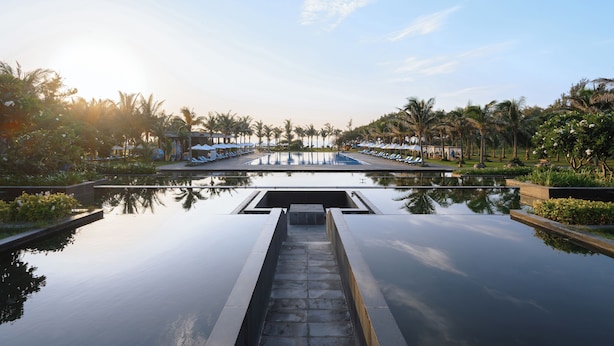 A serene pool area with a clear view of the sky, surrounded by palm trees and lounge chairs. - Muine Bay Resort (Mui Ne)