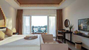 Habitación de hotel con una cama grande, un escritorio, una silla y un balcón con vistas.