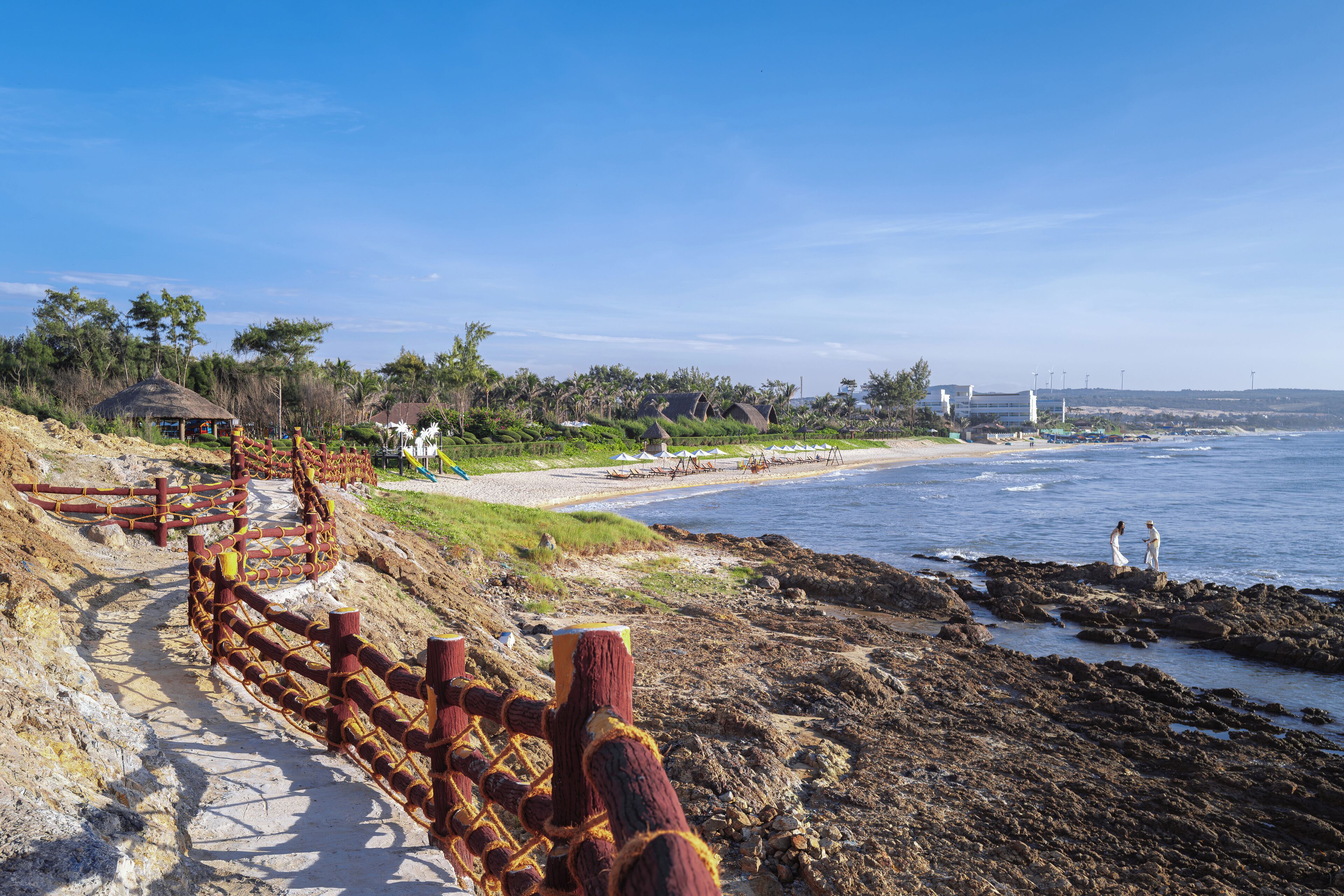 Ein Küstenweg mit Holzzaun, Strand und felsiger Küstenlinie.