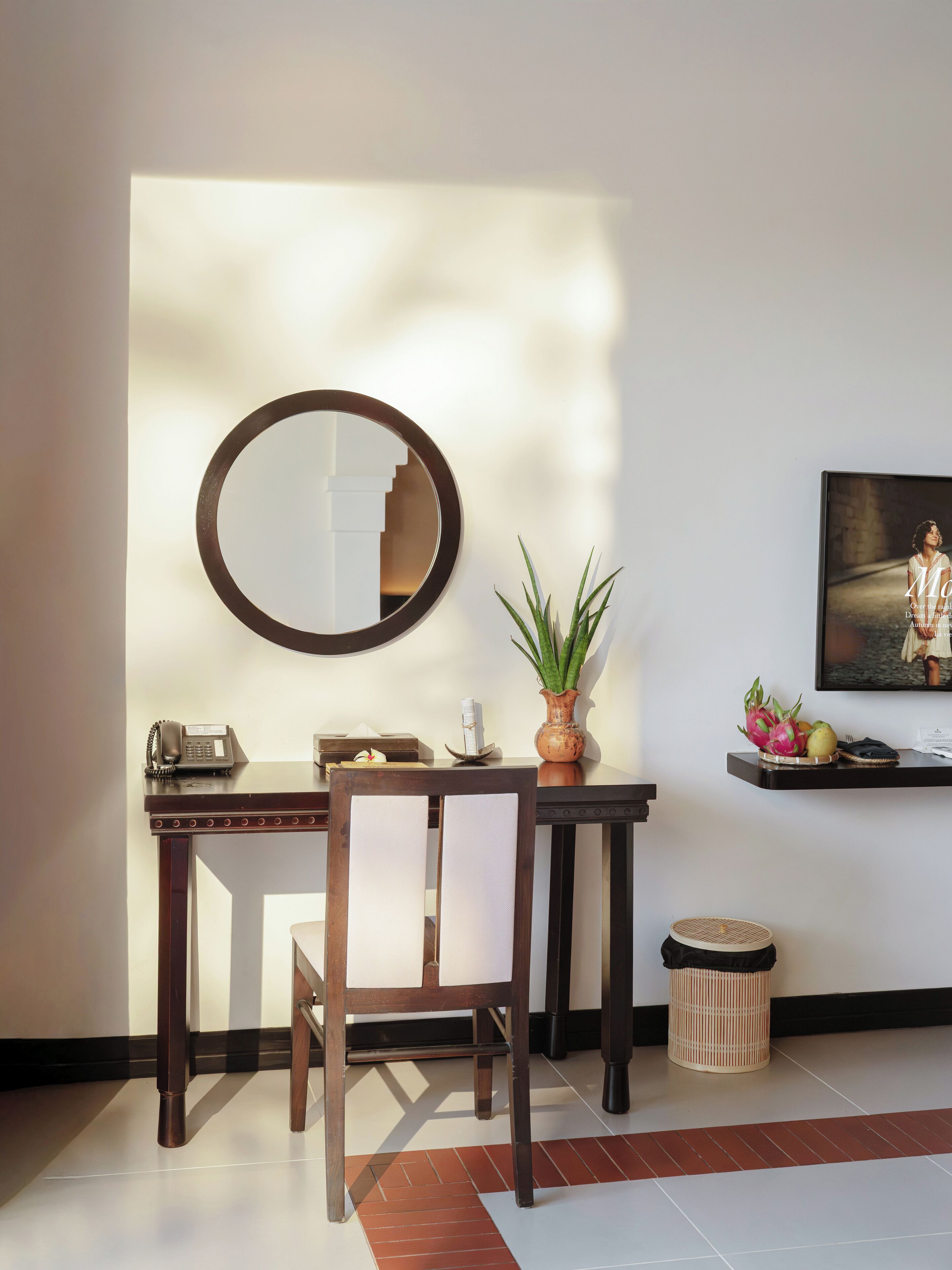 Ein Zimmer mit Schreibtisch, Stuhl, Spiegel, Blumentopf und einem gerahmten Bild an der Wand.