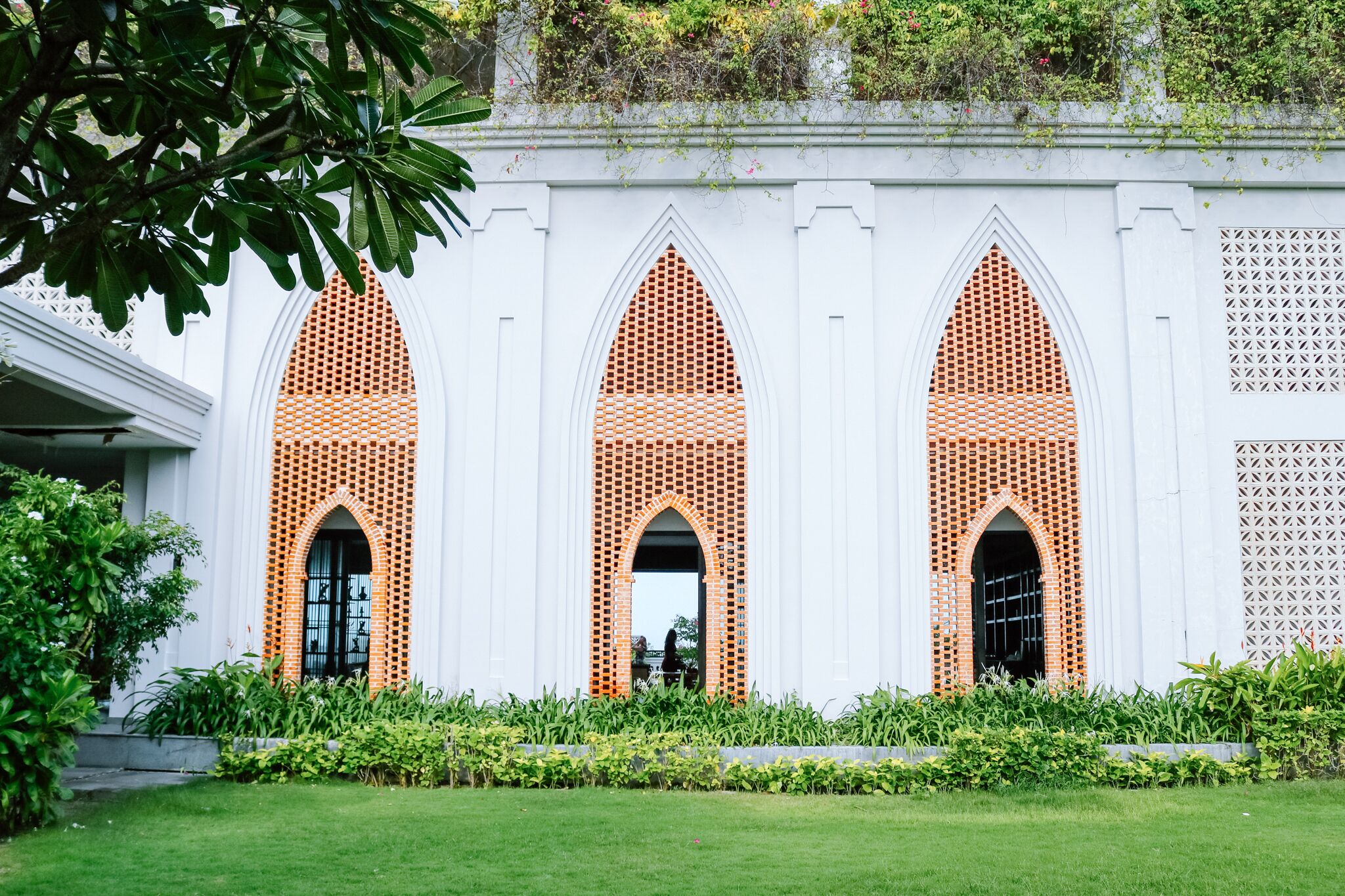 A building with three arched windows with brick patterns, surrounded by a well-maintained garden.