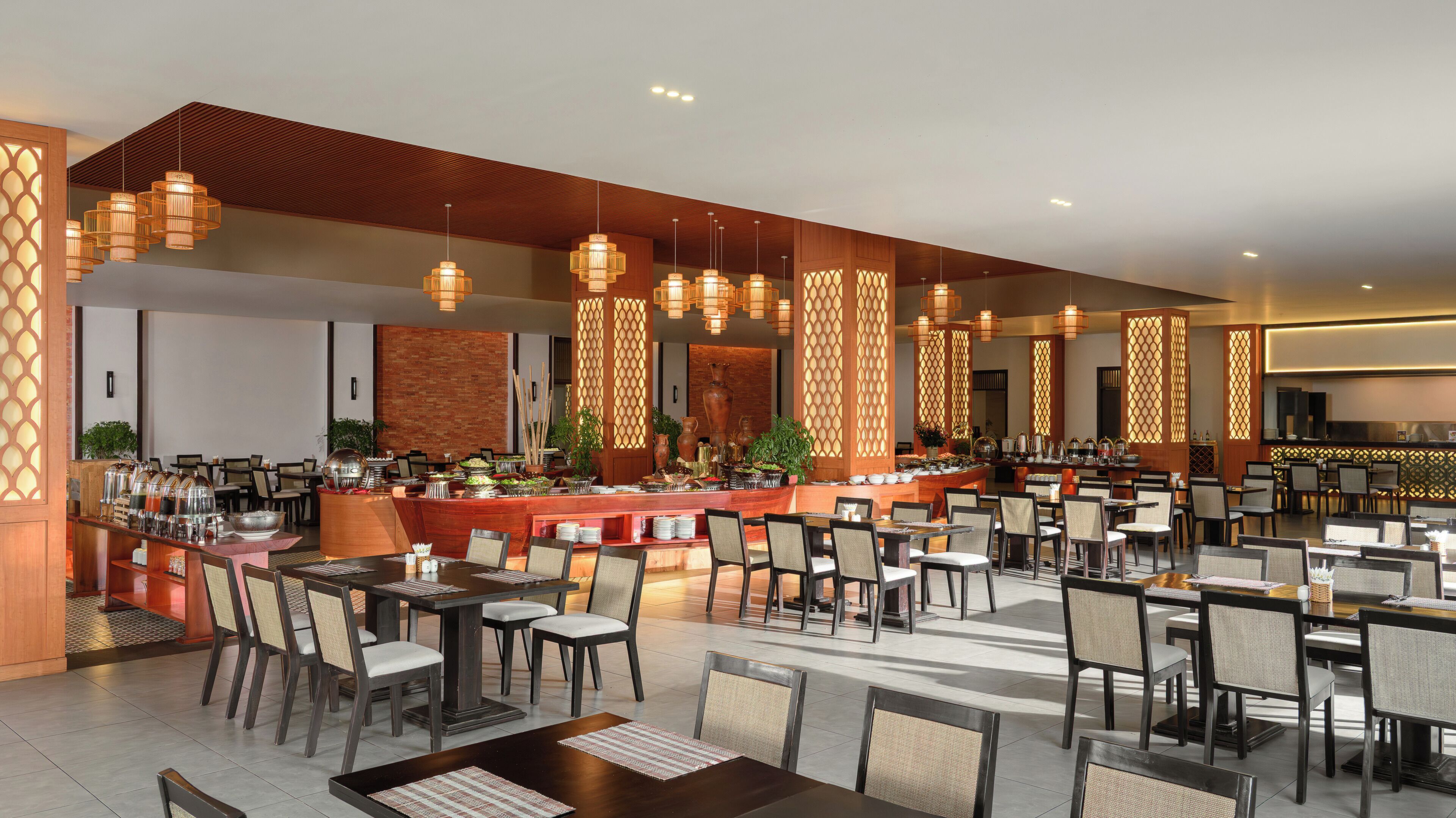 A spacious dining area with multiple tables and chairs, a buffet with various food items, and decorative lighting fixtures.