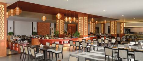 A spacious dining area with multiple tables and chairs, a buffet with various food items, and decorative lighting fixtures.