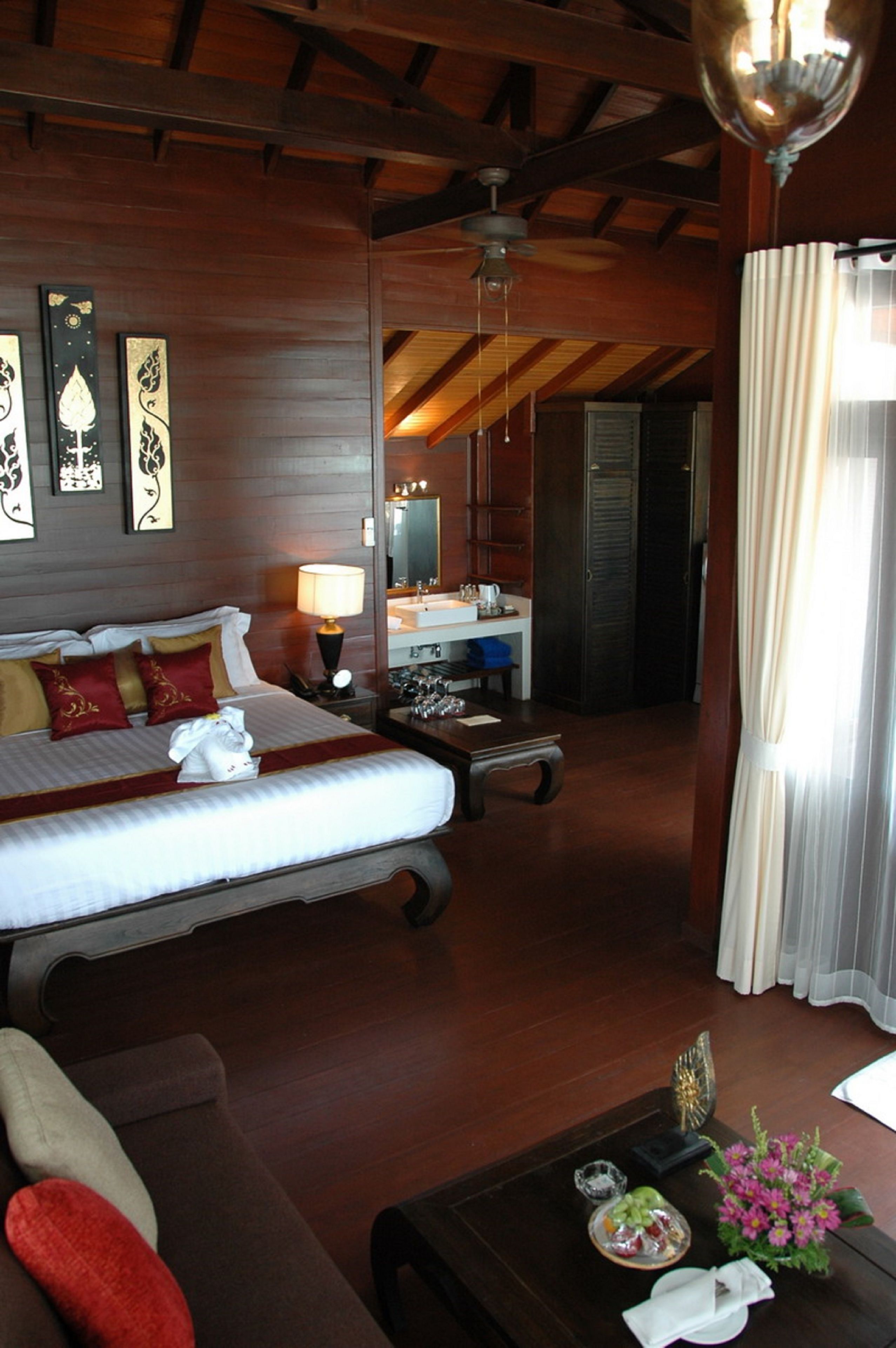 A hotel room with a large bed, a sitting area with a sofa, a small table with a vase and a remote control, and a bathroom visible through an open door.