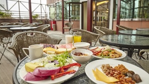 A dining area with outdoor seating, including wicker chairs and round tables, with various dishes and drinks on trays. - Hotel G7 Taipei (New Taipei City)