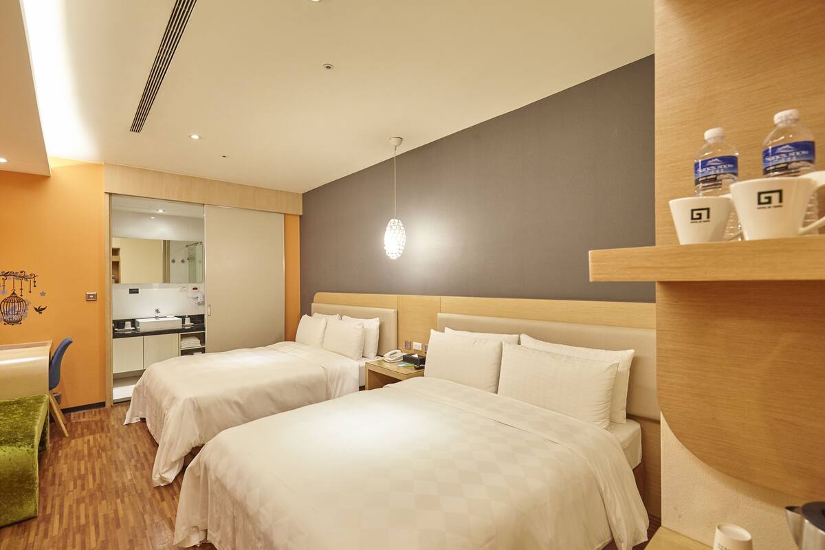 A hotel room with two beds, a desk, a chair, a small kitchenette, and a bathroom.