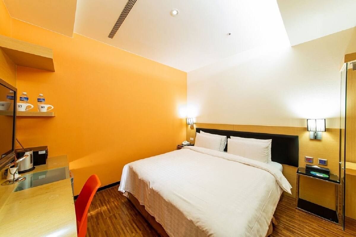 A hotel room with a bed, bedside tables, a desk with a chair, and a coffee station.