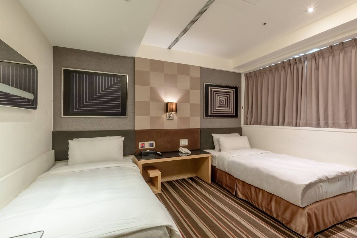 A hotel room with two beds, a nightstand, a lamp, and a wall with geometric artwork.