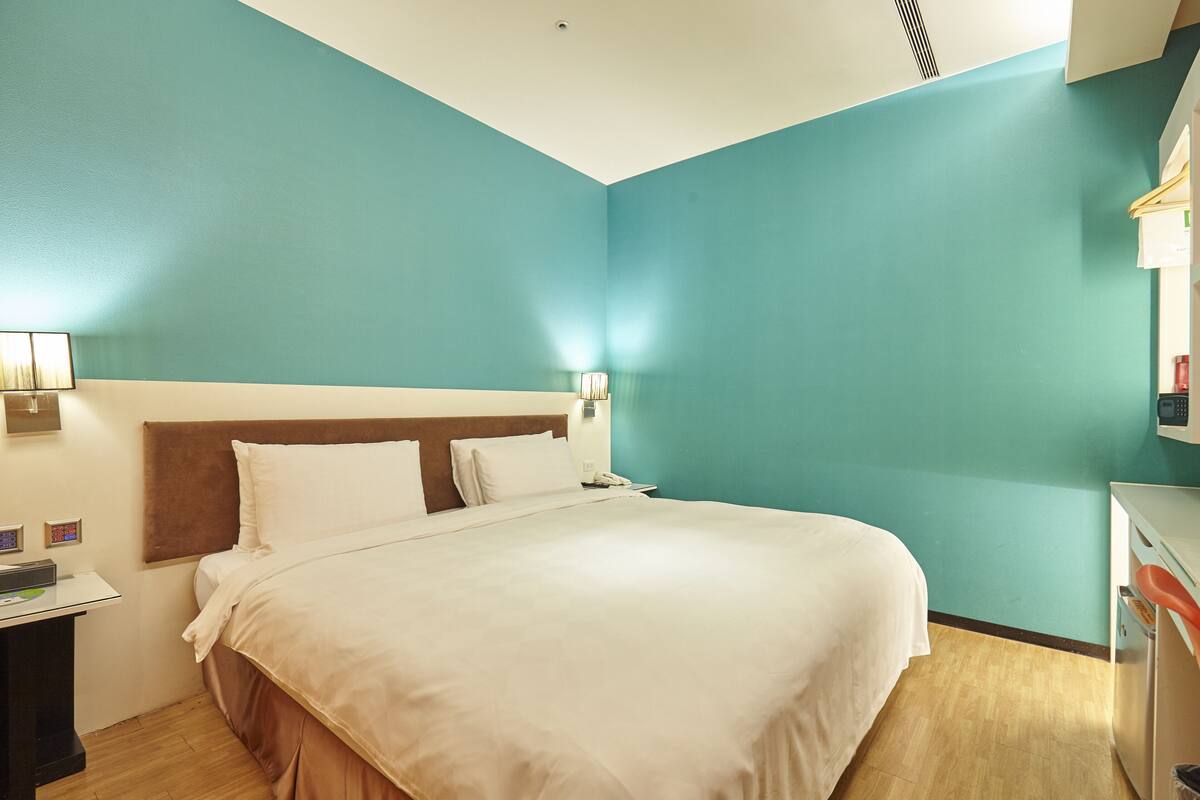 A hotel room with a bed, bedside table, lamp, and a small desk with a telephone.