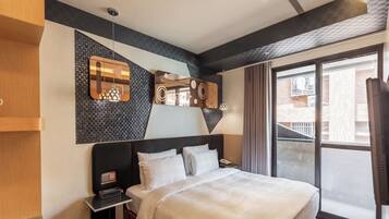 A modern hotel room with a large bed, a nightstand, a mirror, and a window with a view of the city.