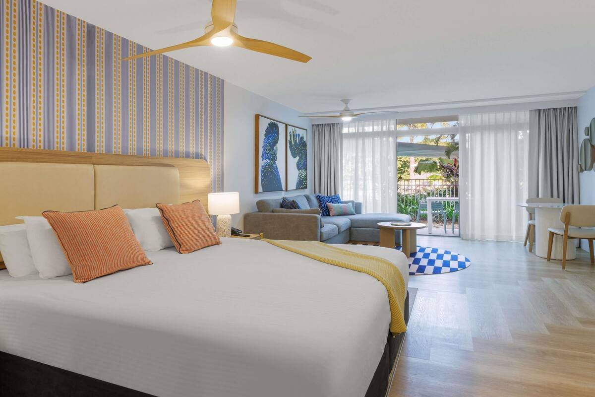 Une chambre d’hôtel avec un grand lit, un canapé, un bureau et un balcon agrémenté d’un tapis à carreaux.