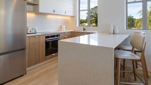 A modern kitchen with wooden cabinets, stainless steel appliances, and a large island with bar stools. - The Sebel Palm Cove (Palm Cove)