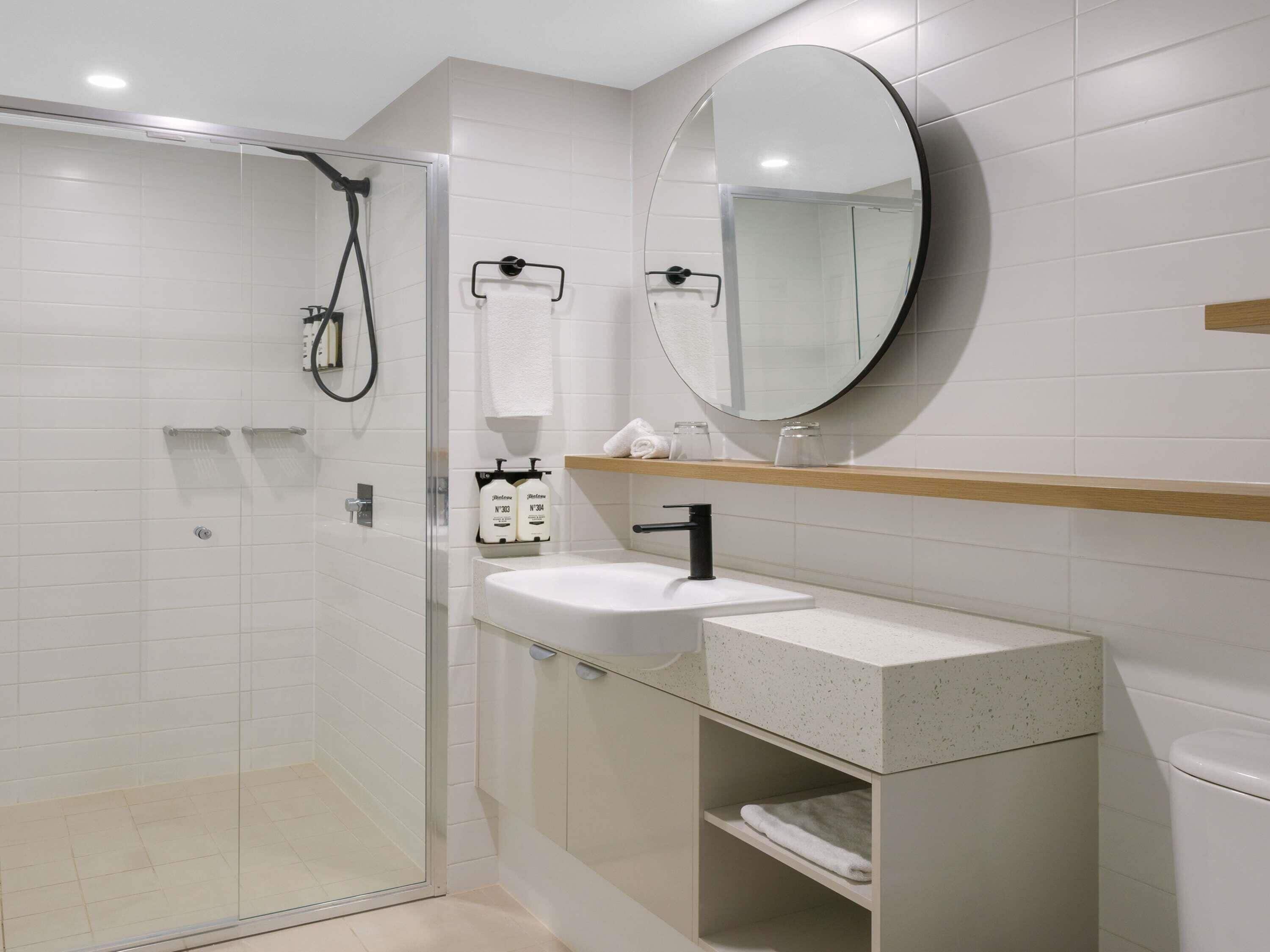 Un baño moderno con cabina de ducha de vidrio, un lavabo blanco y un espejo redondo.