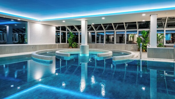 Une piscine intérieure moderne, dotée d’un éclairage géométrique et de grandes fenêtres.