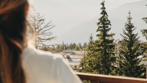 Une personne qui contemple un paysage montagneux, avec des arbres et des bâtiments visibles au loin.