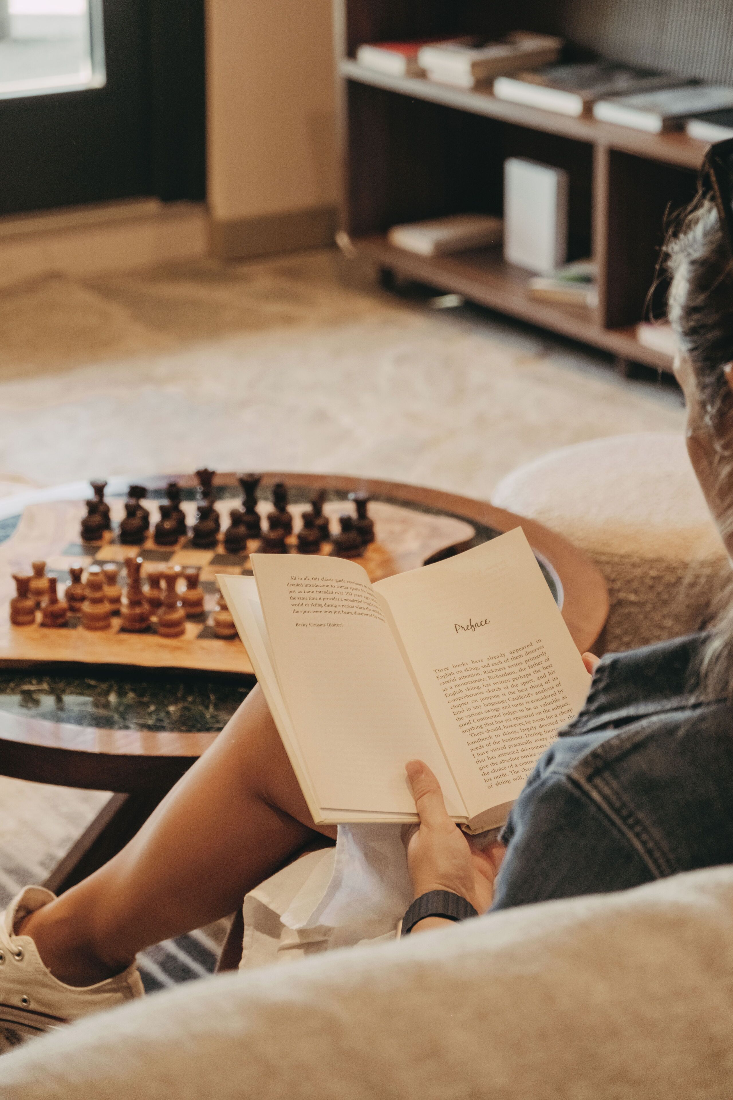 A person reading a book with a chessboard in the background.