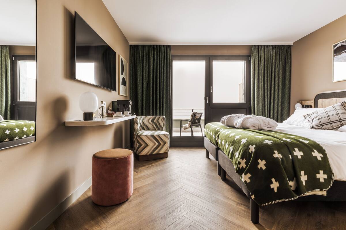 A modern hotel room with a bed, a chair, a small table, and a mirror.