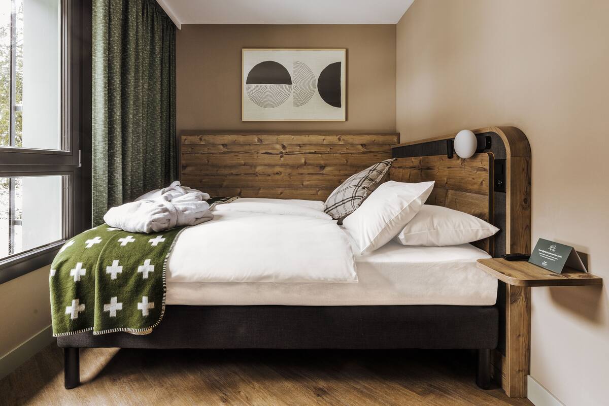A neatly made bed with a green blanket, a wooden headboard, and a bedside table with a lamp and a sign.
