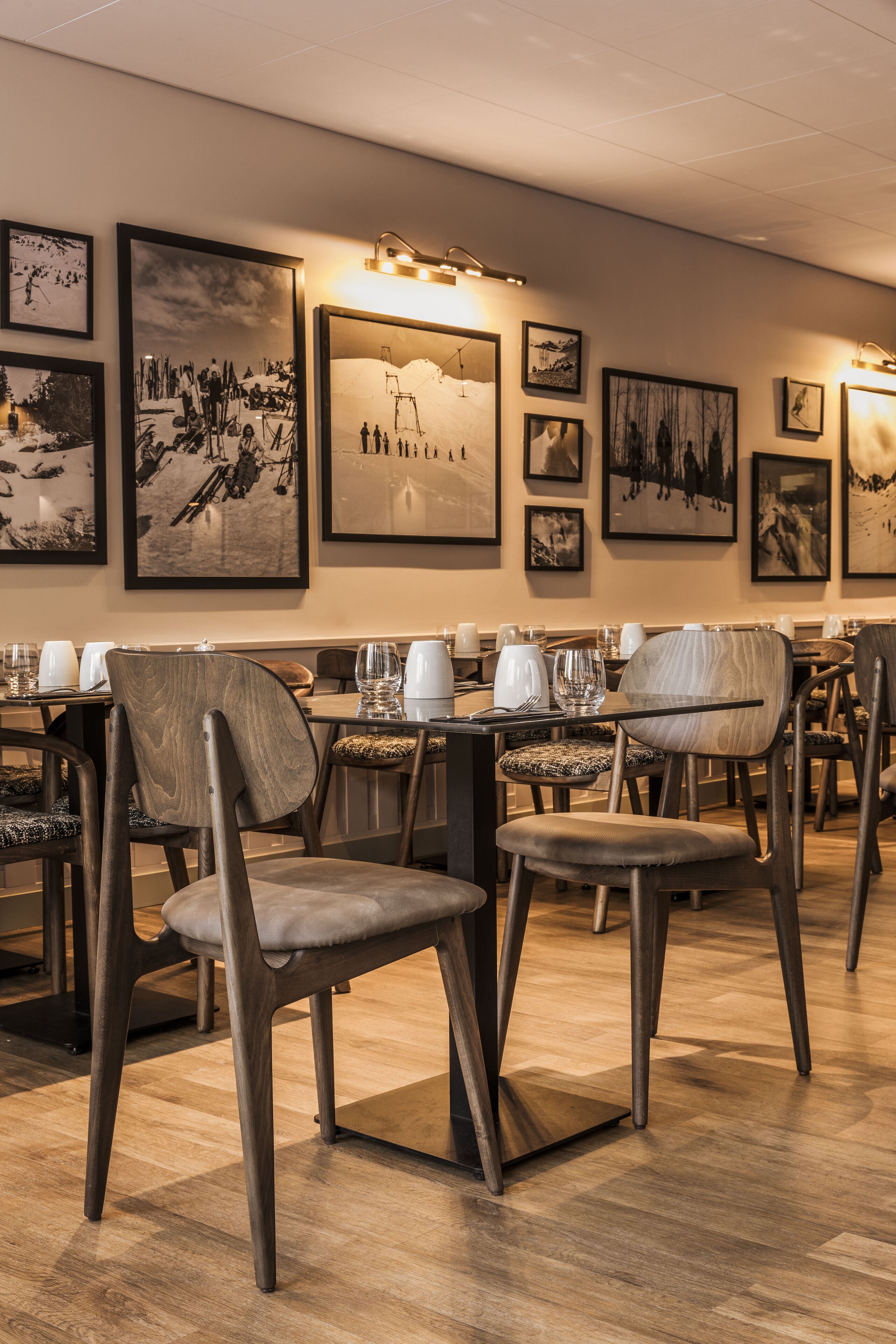 A restaurant with wooden chairs and tables, framed pictures on the wall, and a warm lighting ambiance.