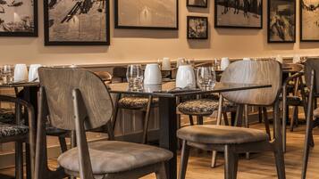 A restaurant with wooden chairs and tables, framed pictures on the wall, and a warm lighting ambiance.