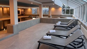 Un espace spa moderne doté d’une piscine, de chaises longues et d’un mur en pierre.