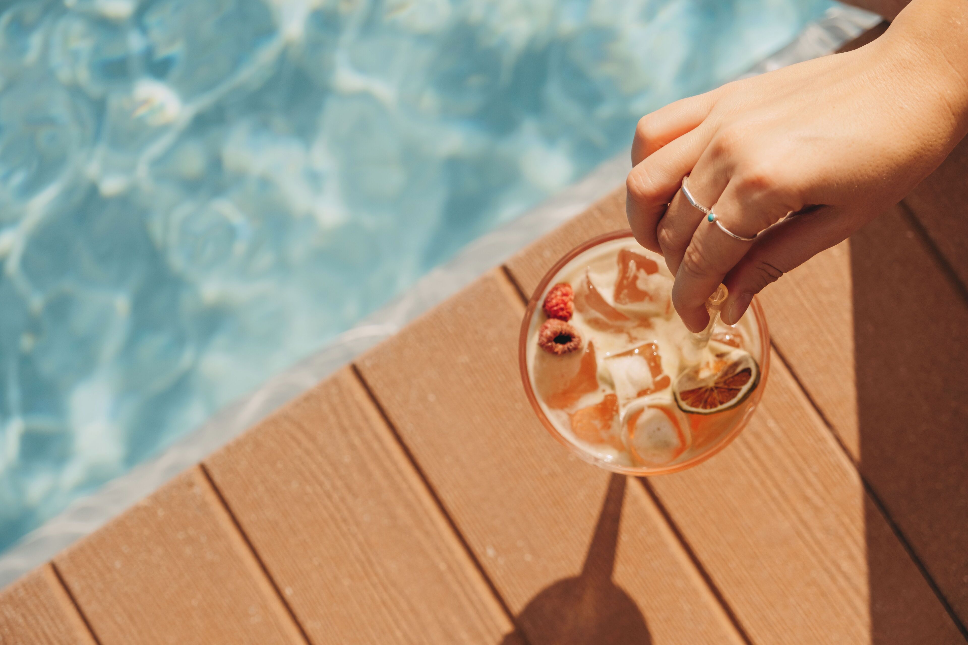 A hand holding a drink near a pool.