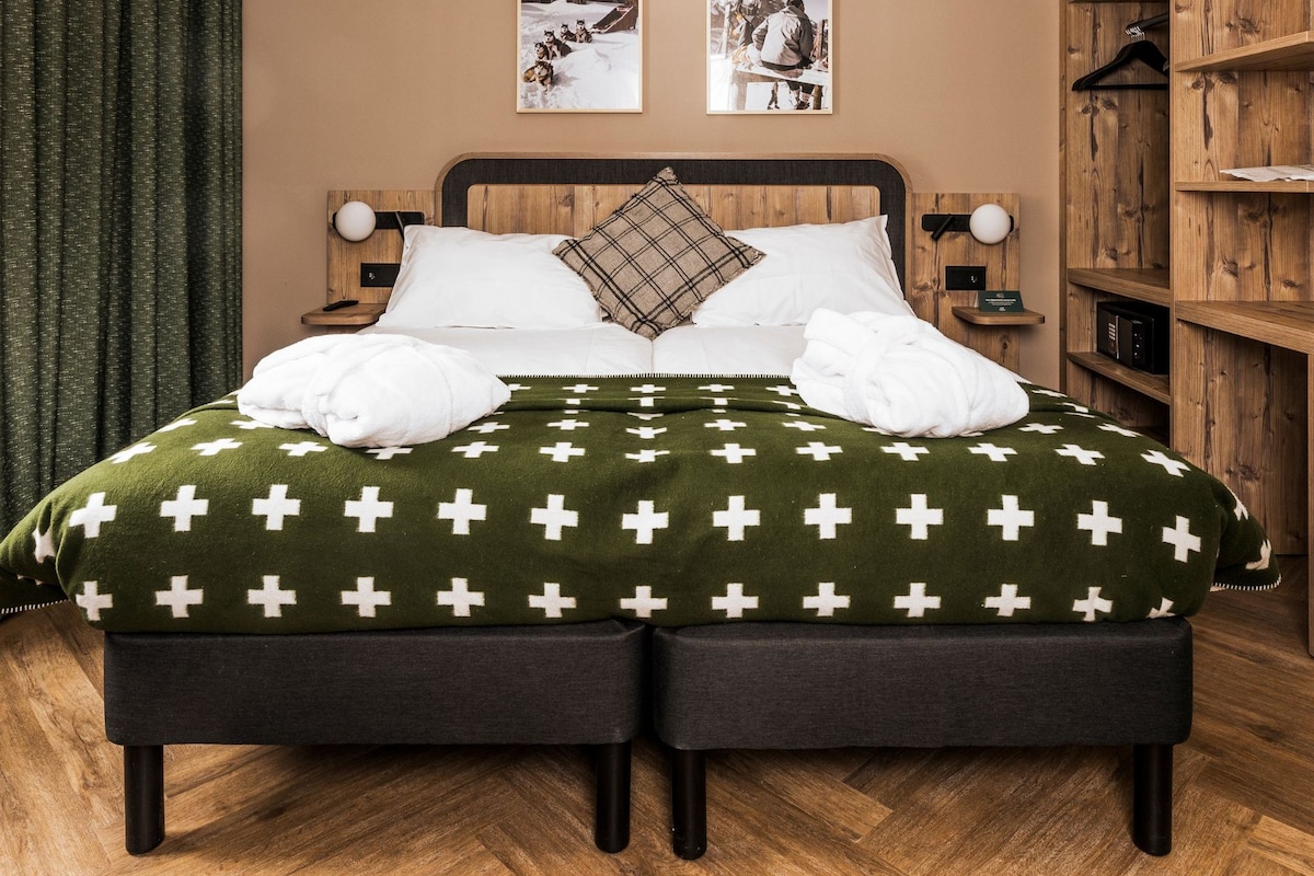 Un lit double avec une couverture verte, deux tables de chevet avec des lampes, une armoire en bois et deux tableaux encadrés accrochés au mur.