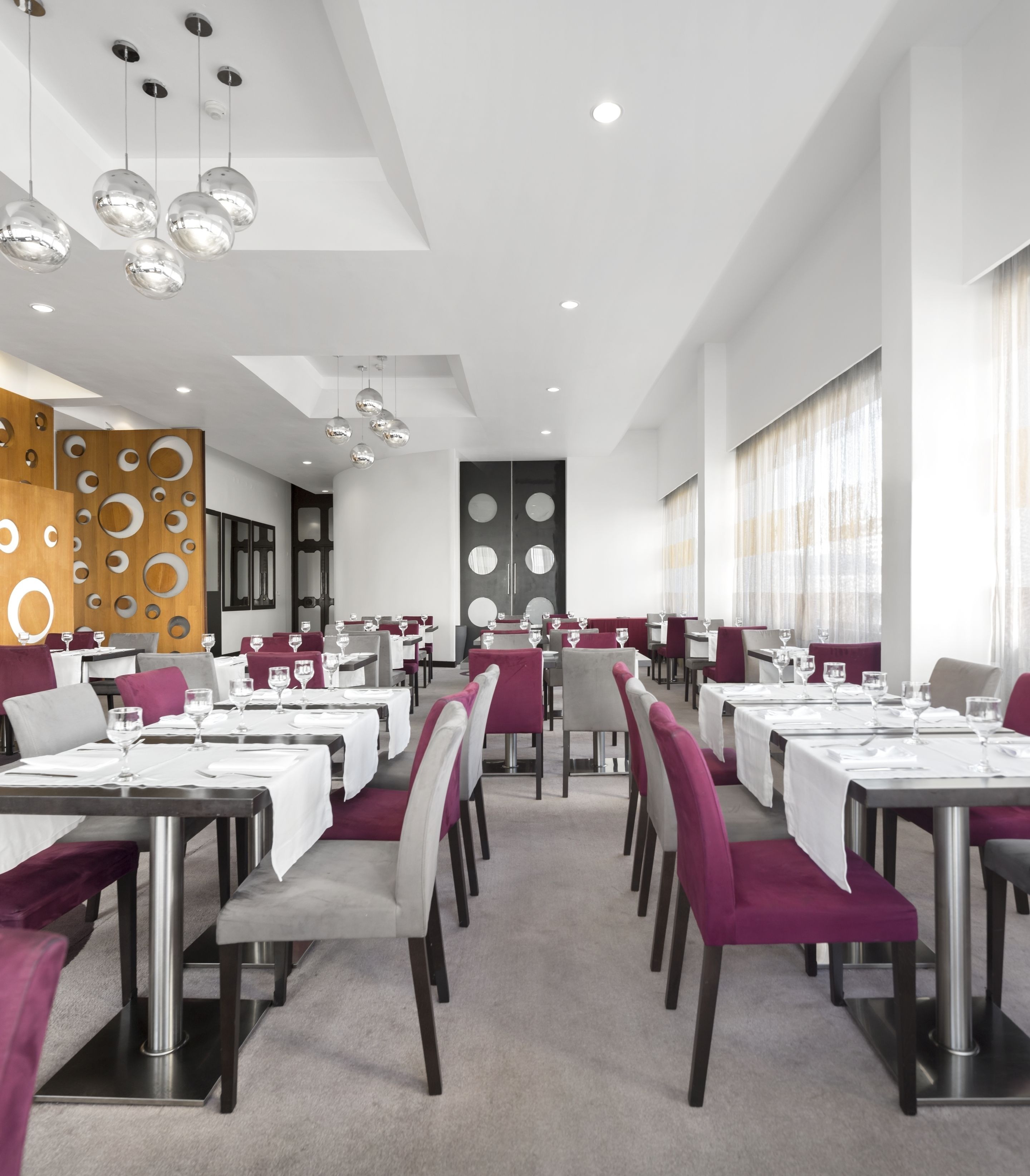 Un restaurant moderne avec des tables blanches, des chaises violettes et un plafond orné de luminaires sphériques suspendus.