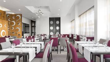Un ristorante moderno con tavoli bianchi, sedie viola e un soffitto con luci sferiche sospese.