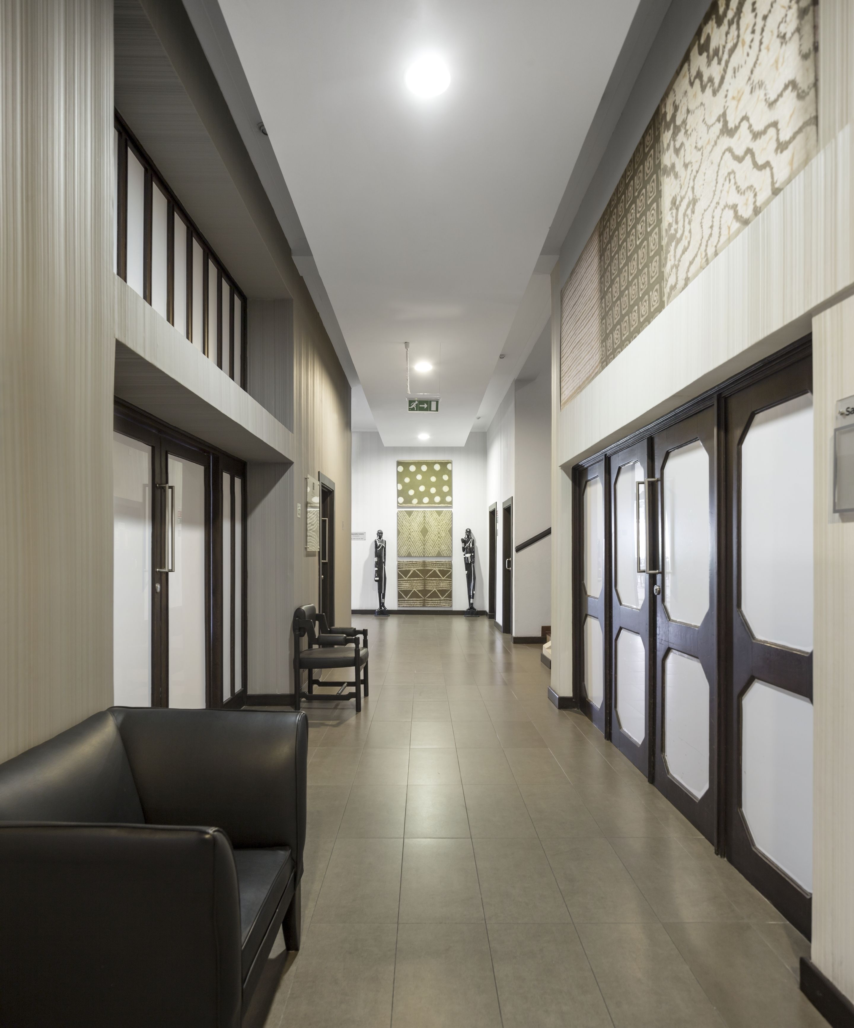 A modern hallway with a long corridor, two seating areas with chairs, and a patterned wall at the end.