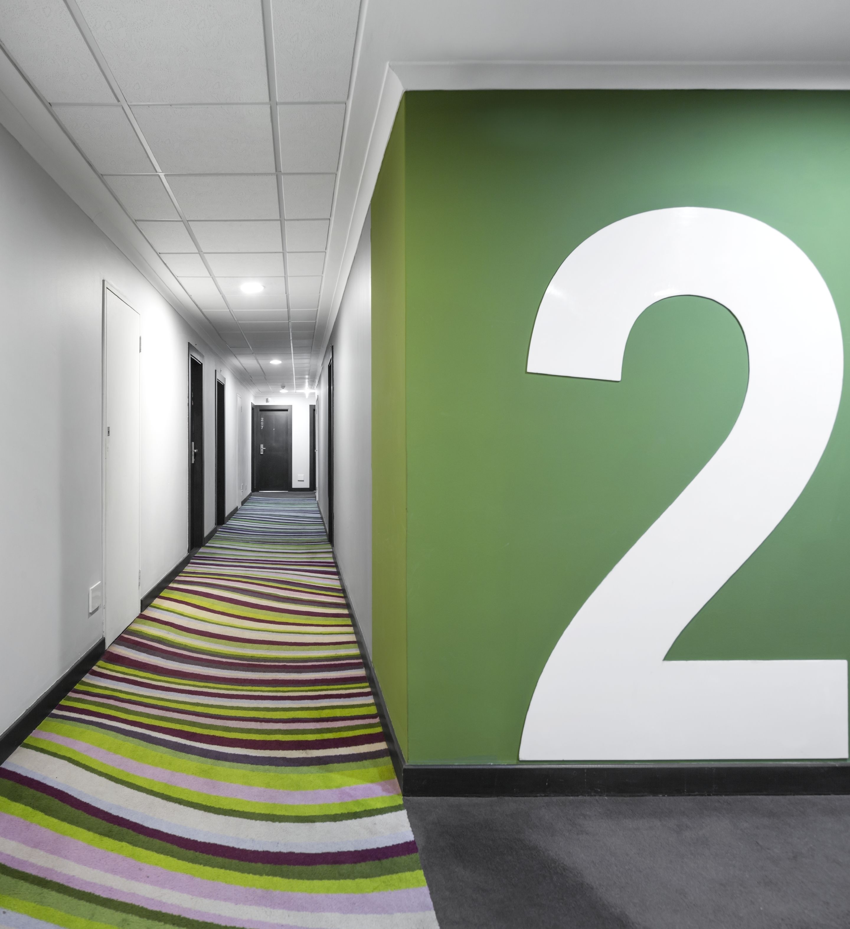 Un pasillo con alfombra a rayas, paredes blancas y el número 2 grande, pintado en blanco sobre una pared verde.