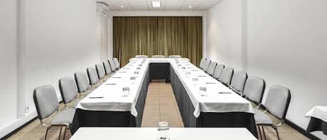 Un salón de conferencias con una larga mesa, sillas y un telón de fondo.