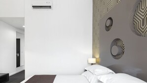 A modern hotel room with a large bed, a bedside table with a lamp, a wall-mounted air conditioner, and a patterned wall design.