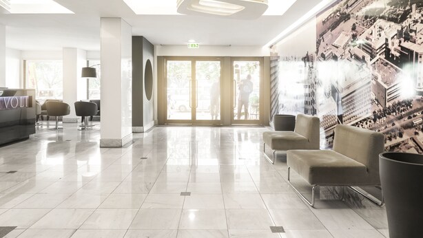 A modern lobby with a glass ceiling, a reception desk, seating area, and a mural of a cityscape.
