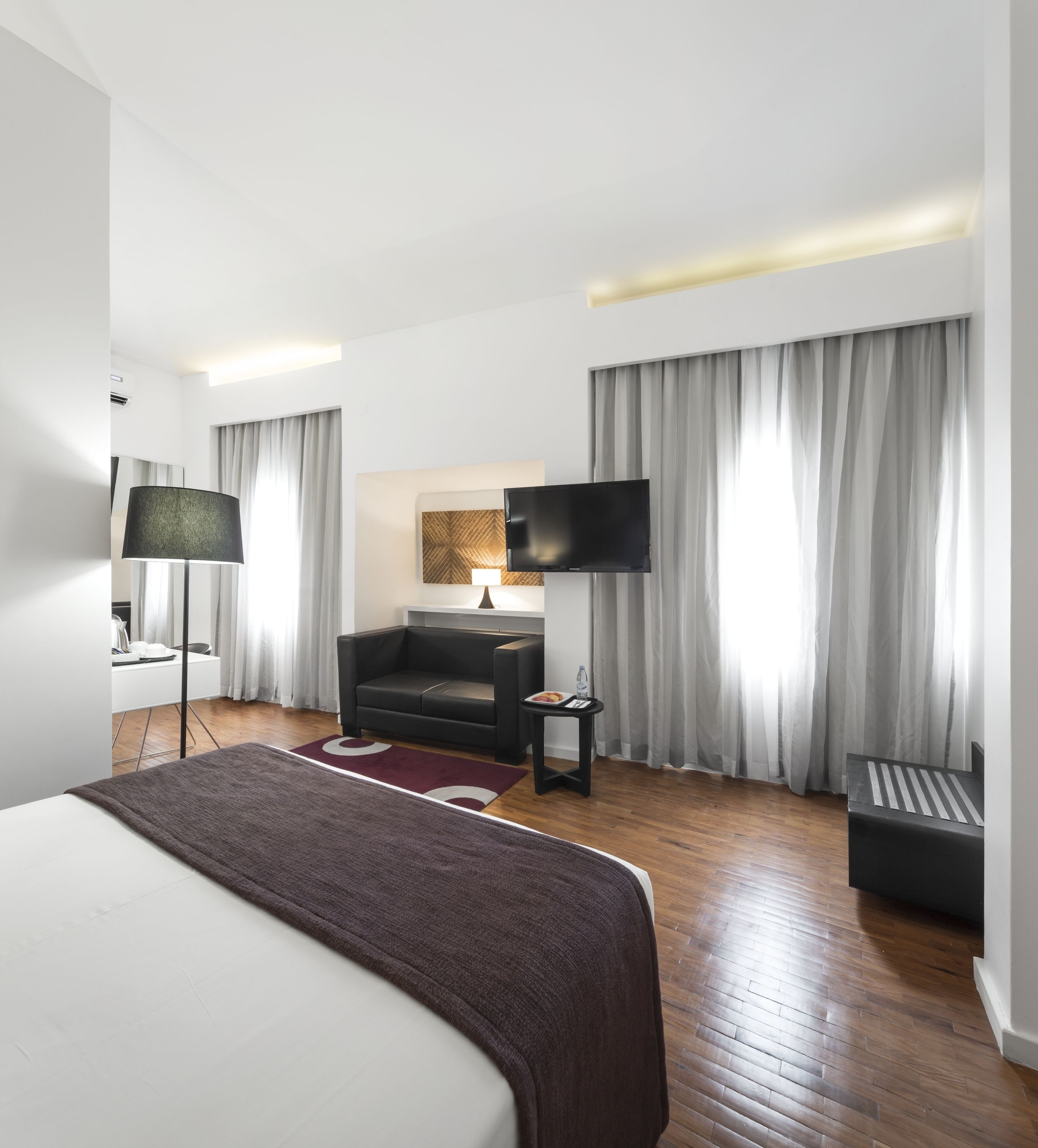 A modern hotel room with a large bed, a flat-screen TV, a sofa, a small table, and a desk.