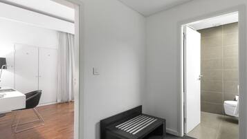 Una habitación moderna y minimalista con un banco oscuro, un escritorio blanco y una puerta de baño a la vista.