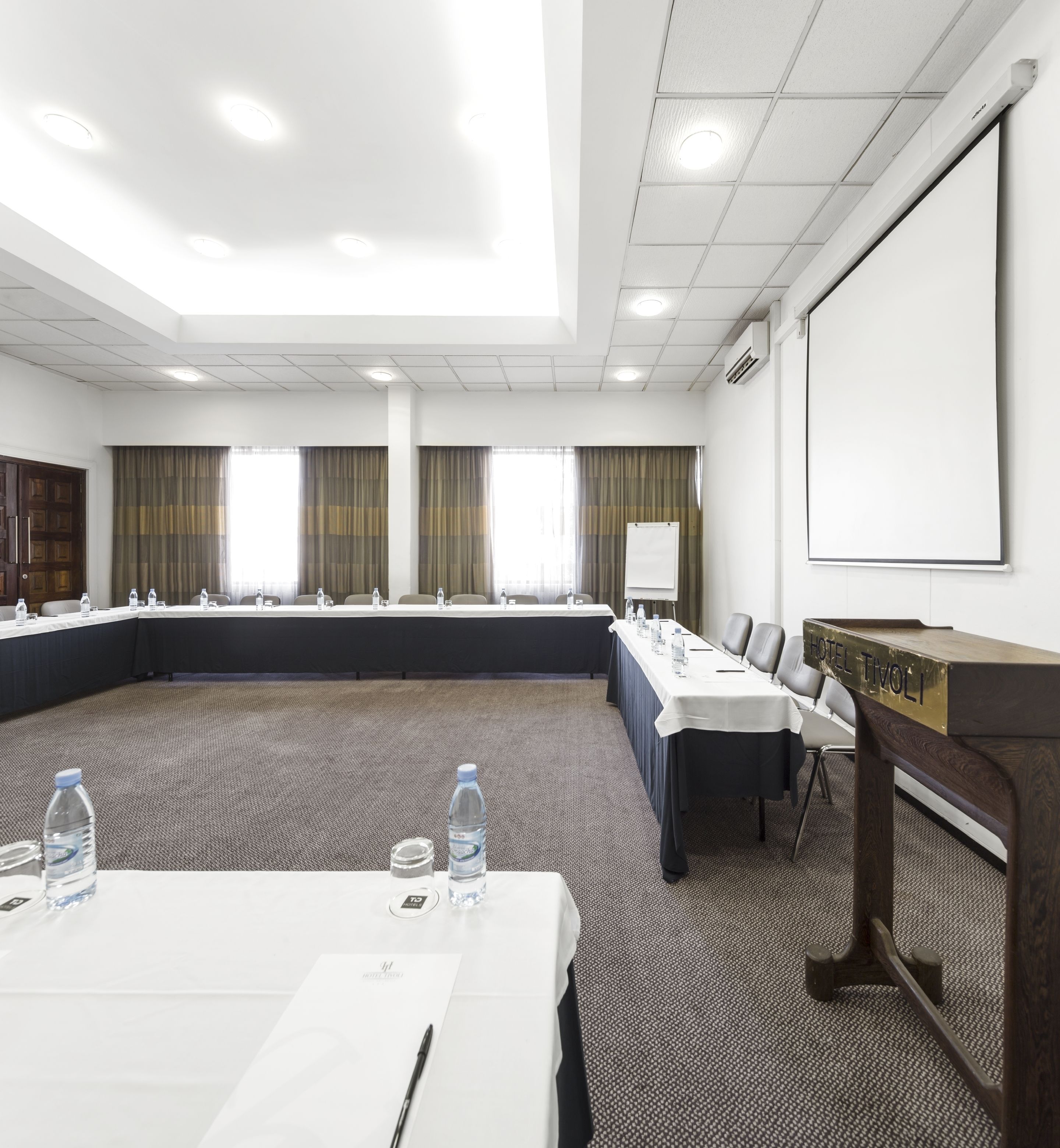 Ein Konferenzraum mit langem Tisch, Stühlen, einem Rednerpult und einer Projektionsleinwand.