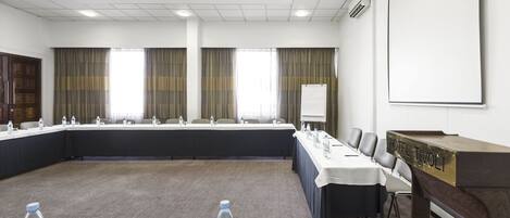 A conference room with a long table, chairs, a podium, and a projector screen.