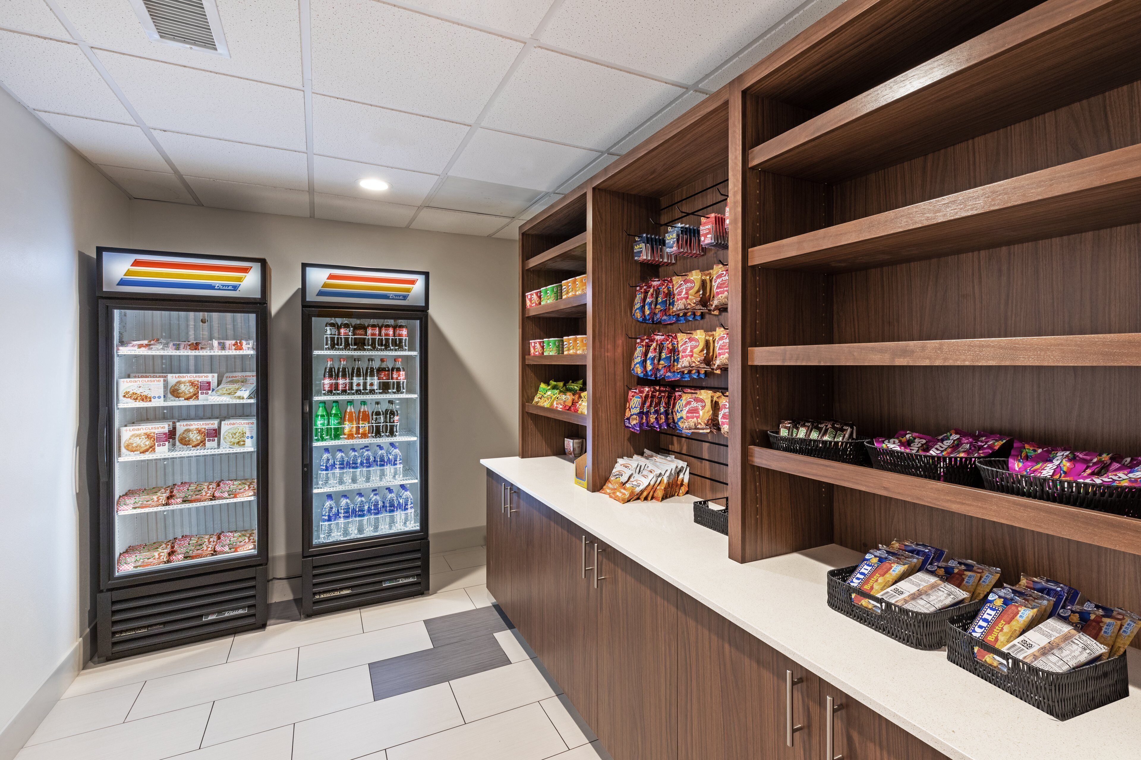 A self-service snack and beverage station with refrigerated drink dispensers and shelves stocked with snacks and packaged goods.