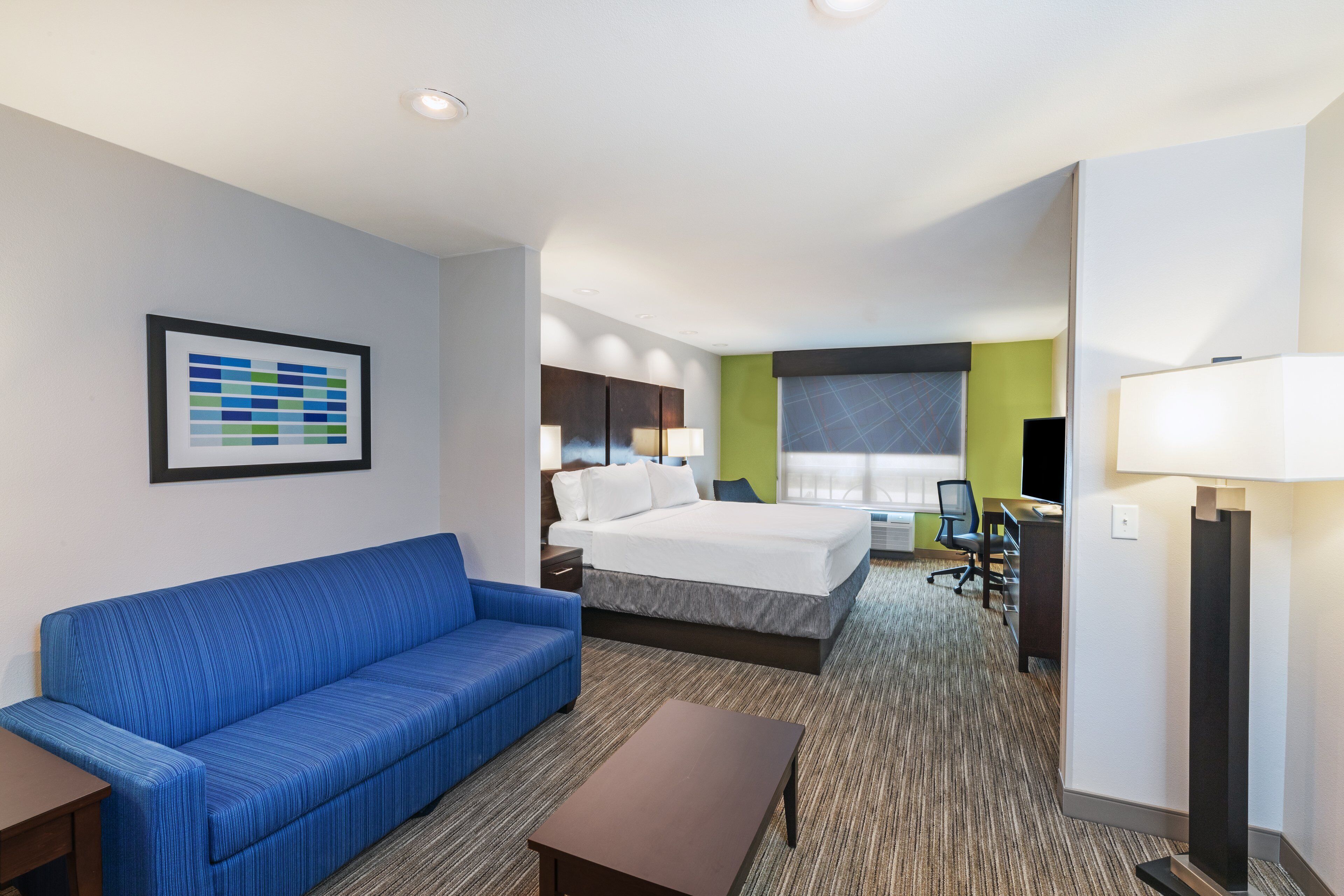 Une chambre d’hôtel avec un canapé bleu, un lit, un bureau et une lampe.