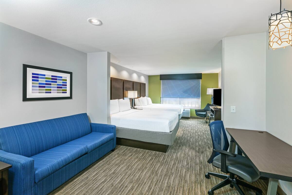 A hotel room with a blue sofa, two beds, a desk, and a framed color chart on the wall.