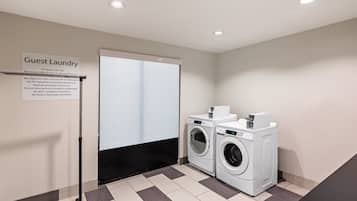 Un espace buanderie à la disposition des clients, comprenant deux machines à laver, un étendoir et un panneau indiquant les instructions d’utilisation.