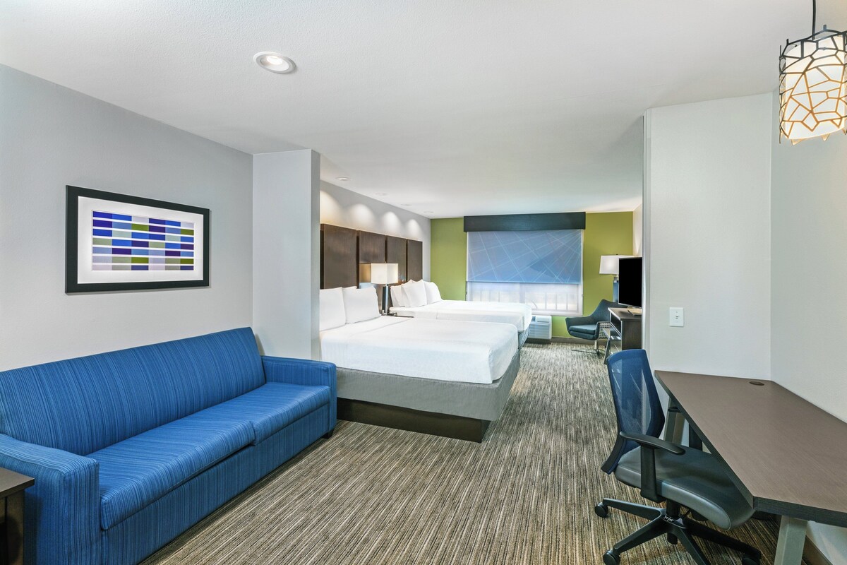 A hotel room with a blue sofa, two beds, a desk, and a chair.
