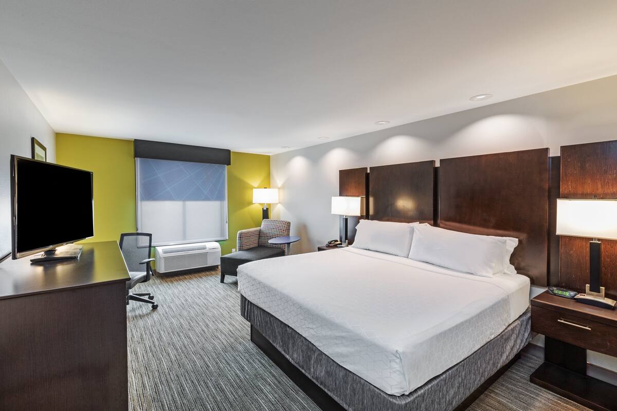 A hotel room with a large bed, a desk, a chair, a TV, and two lamps.