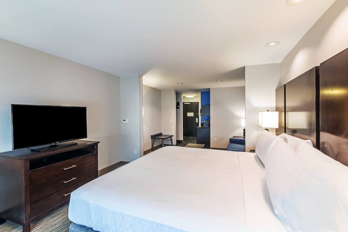 A hotel room with a large bed, a flat-screen TV on a wooden dresser, and a desk with a chair.
