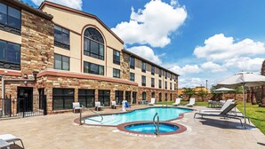 A hotel with a swimming pool, outdoor seating, and a stone facade.