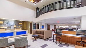 A modern hotel lobby with a reception desk, seating area, and a staircase.